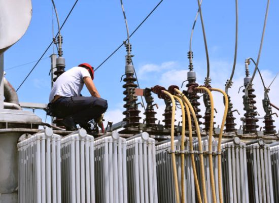 Manual worker in protective workwear and hard hat repairing electricity equipment in power plant